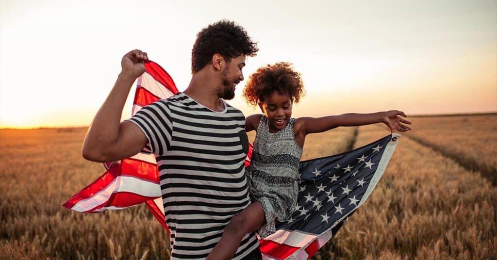 father and daughter in wheat field with American flag