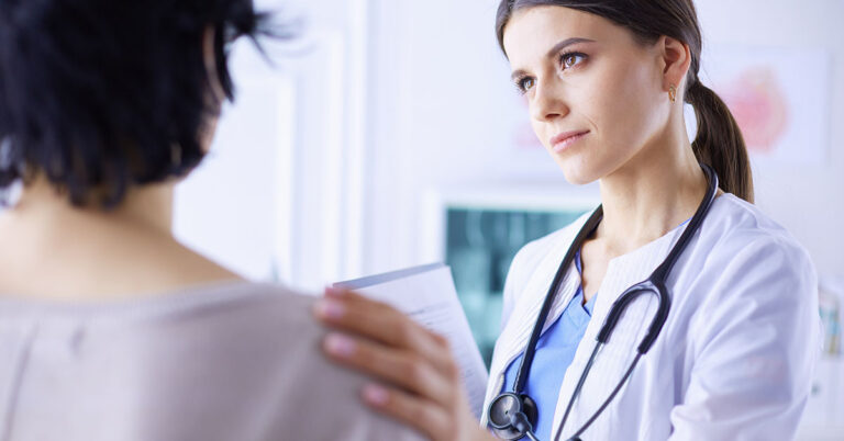 A doctor in a white coat listens attentively to a patient, showing concern and care in a medical setting.