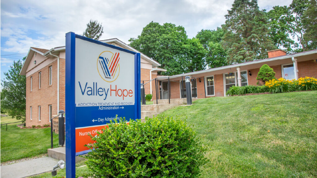 A brick building with a sign for "Valley Hope," an addiction treatment and recovery center, surrounded by greenery.