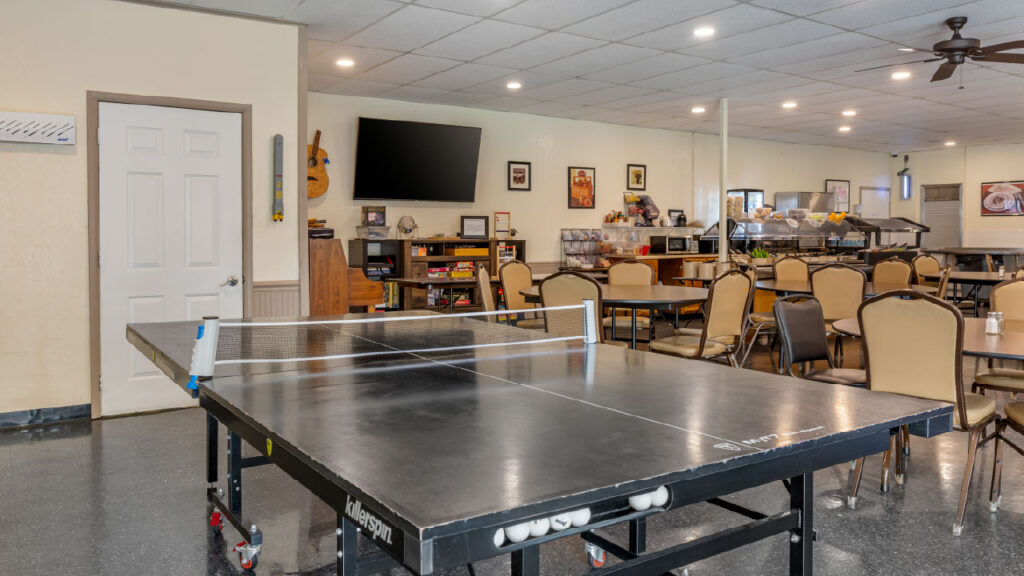 A spacious dining area featuring a ping pong table, chairs, and a TV on the wall, with a buffet setup in the background.