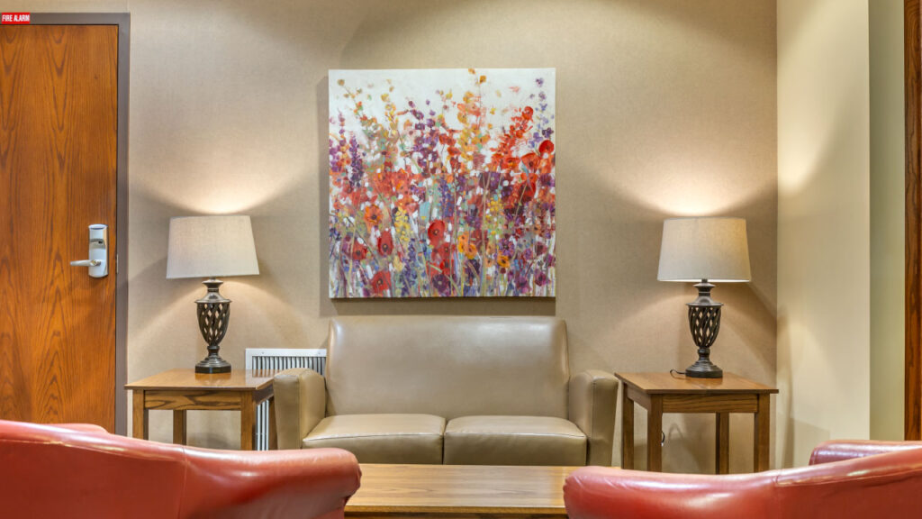 A cozy seating area with a light brown sofa, two side tables, lamps, and a colorful floral painting on the wall.
