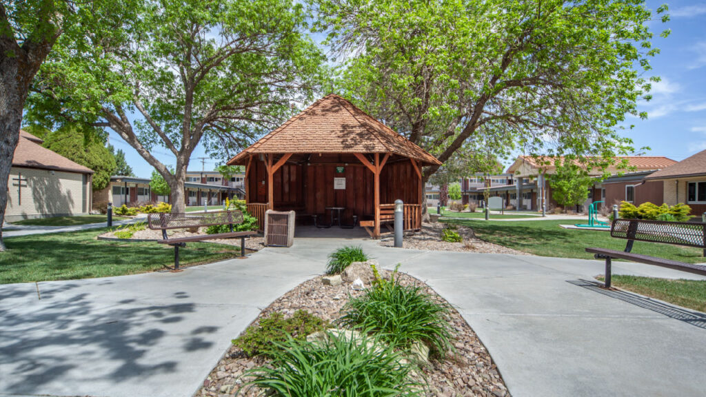 A landscaped courtyard featuring a wooden gazebo, benches, and pathways surrounded by trees and greenery.