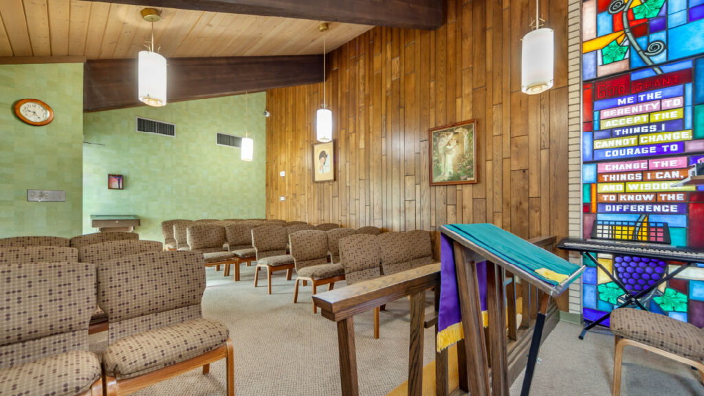 A serene interior of a small chapel featuring wooden walls, seating, and a colorful stained glass window with inspirational text.