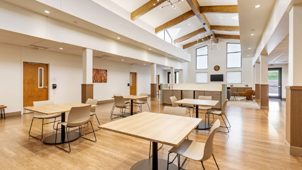 A spacious, modern interior with high ceilings, wooden beams, and several tables and chairs arranged for seating.