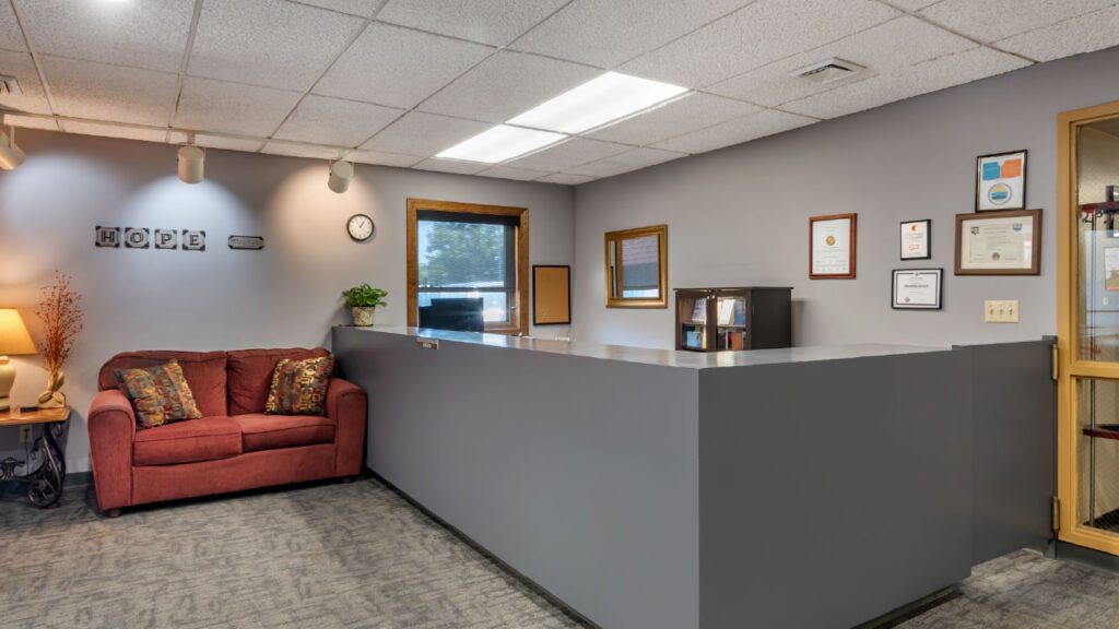 A cozy office reception area featuring a red couch, a clock, and framed certificates on the wall. A welcoming atmosphere.