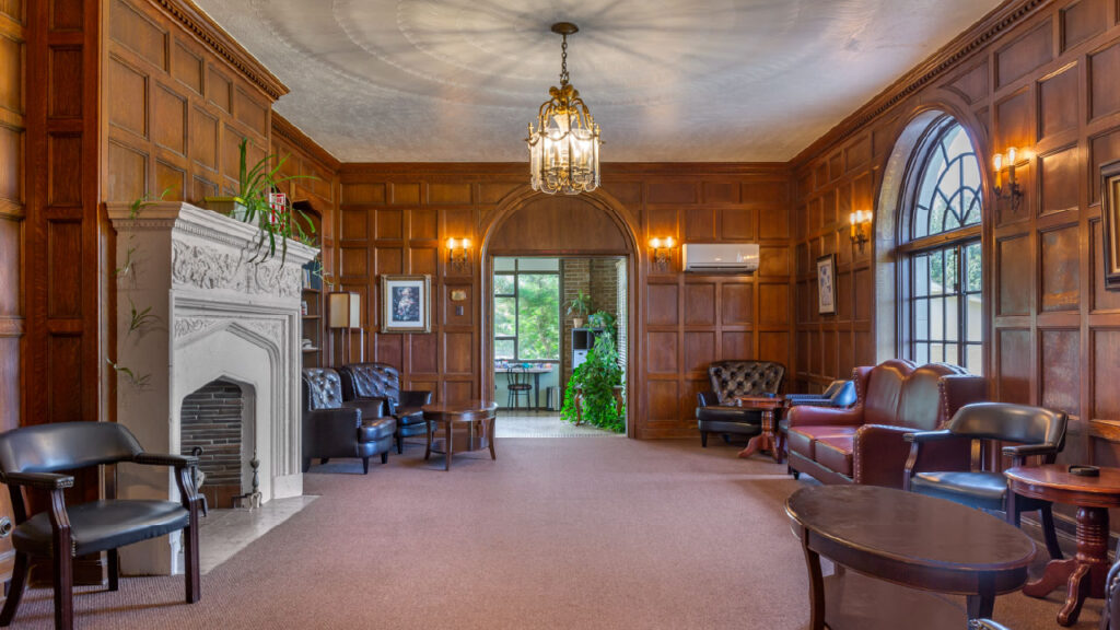 A cozy room with wooden paneling, a fireplace, leather seating, and large windows, creating an inviting atmosphere.