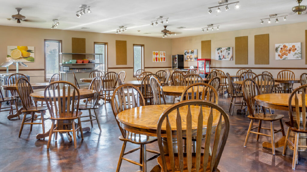 A spacious dining area with wooden tables and chairs, featuring artwork on the walls and a serving station in the background.