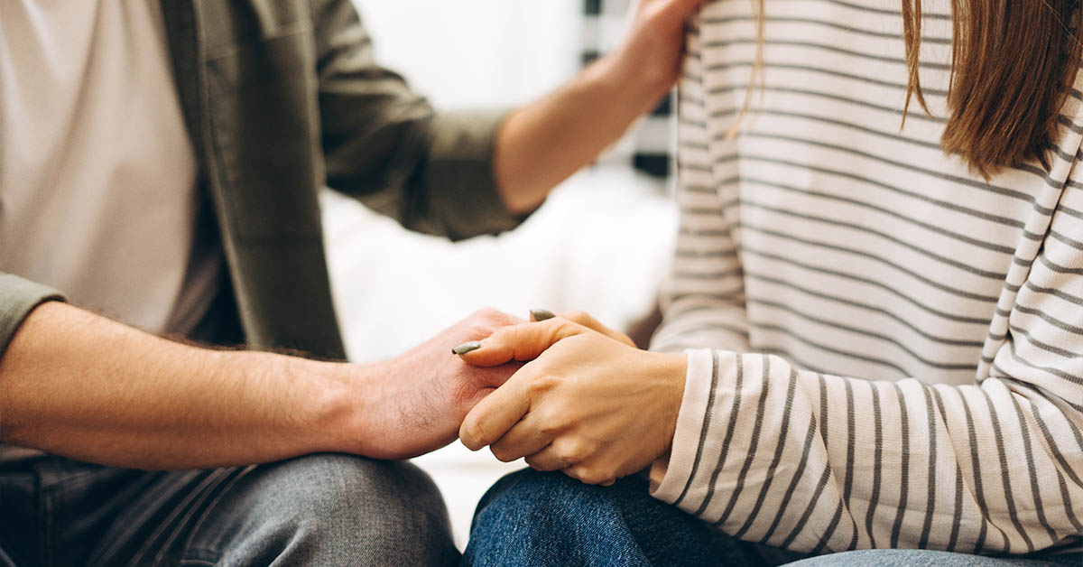 A close-up of two hands holding each other, conveying support and comfort, with a soft background.